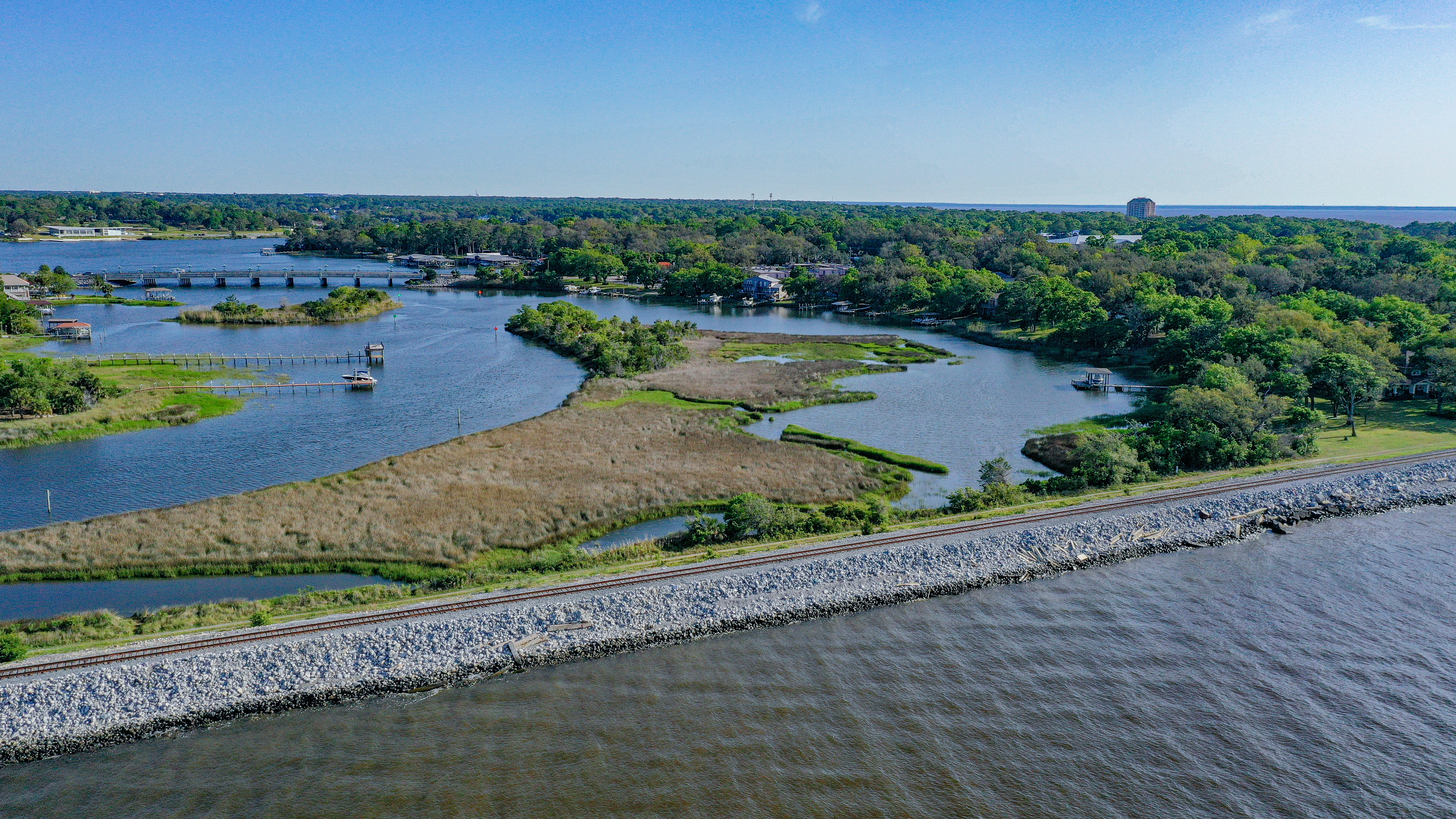 Aerial view of the Bluffline corridor along the bay, with railroad tracks, riprap shoreline, and lush waterfront greenery